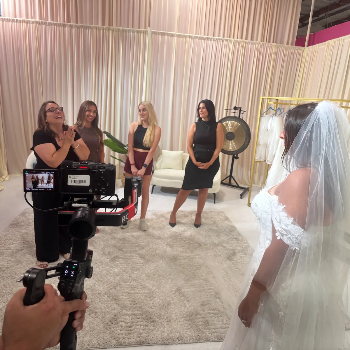 The New York Bride & Groom team cheers as the bride sees her gown in the surprise bridal salon, with a camera rolling